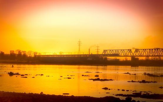 Cityscape by the river with a bridge against the backdrop of the sunset.