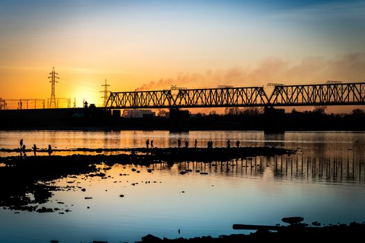 Cityscape by the river with a bridge against the backdrop of the sunset.