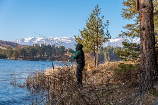 A male fisherman on the lake is standing in the water and fishing for a fishing rod. Fishing hobby vacation concept. Copy space.