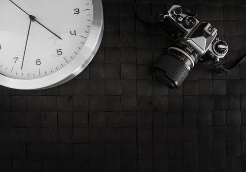 The frenzy of today's times in contrast with the past. A modern design wall clock next to a vintage camera on a black background