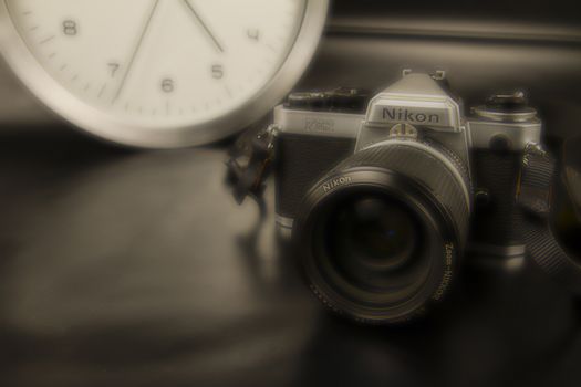 The frenzy of today's times in contrast with the past. A modern design wall clock next to a vintage camera on a black background with sepia and orton effects
