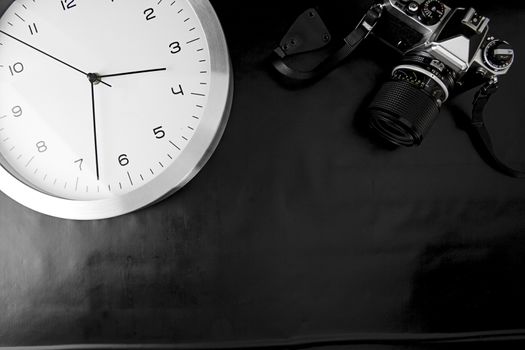 The frenzy of today's times in contrast with the past. A modern design wall clock next to a vintage camera on a black background