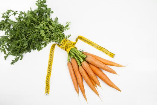 Vegetarian diet to reduce weight. A bunch of freshly picked carrots wrapped in a body measuring tape ruler which symbolizes the waistline