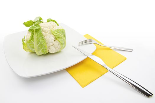 Natural food, a healthy habit. A nice raw cauliflower resting on a plate with cutlery and napkin