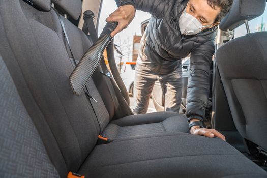 vacuuming the interior of a passenger car using an industrial vacuum cleaner. man works in protective medical mask. protection against coronavirus.