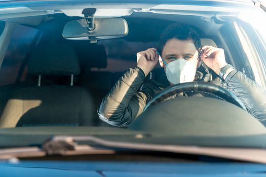 man puts medical mask on face in car. prevention against coronavirus covid-19. quarantine at the time of the viral epidemic.