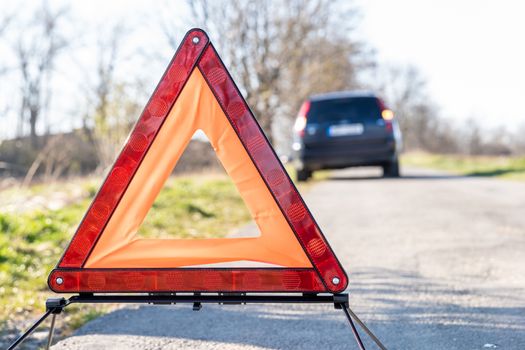 red warning triangle on the road in front of a broken car.