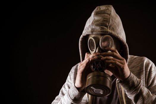 man puts on gas mask to protect against gas. Portrait on black background, dramatic coloring.
