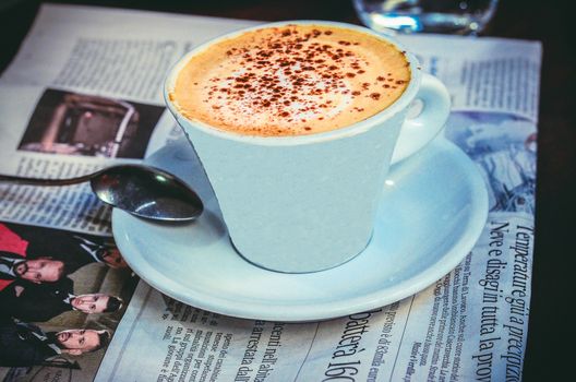 A cup of freshly brewed cappuccino on the table with newspaper