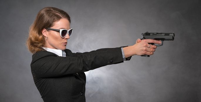 Portrait of woman with gun on grey background.