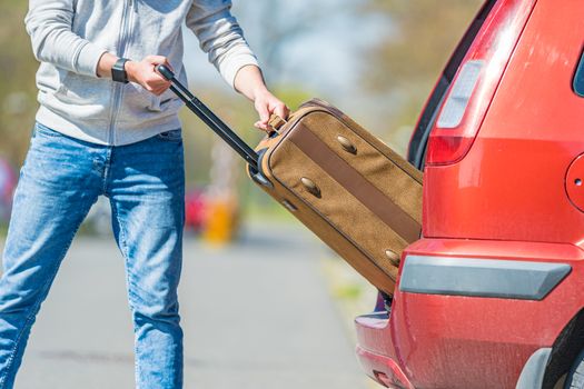 A young man pulls his luggage out of the trunk of a car.