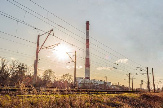 High pipe of thermal power station near the railway at sunset