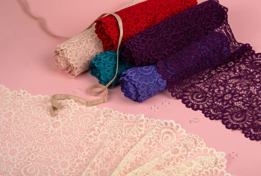 Roll of Delicate color laces for panties and bras on pink background with plastic fittings. Elastic material. Using for Atelier and fabric store.