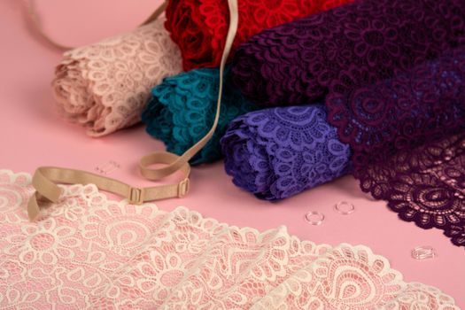 Roll of Delicate color laces for panties and bras on pink background with plastic fittings. Elastic material. Using for Atelier and fabric store.