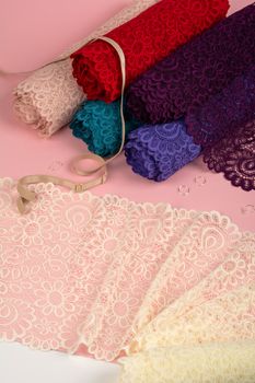 Roll of Delicate color laces for panties and bras on pink background with plastic fittings. Elastic material. Using for Atelier and fabric store.