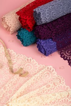 Roll of Delicate color laces for panties and bras on pink background with plastic fittings. Elastic material. Using for Atelier and fabric store.