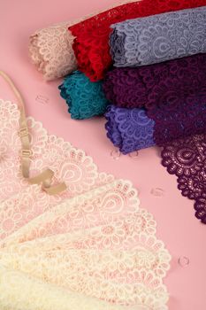 Roll of Delicate color laces for panties and bras on pink background with plastic fittings. Elastic material. Using for Atelier and fabric store.