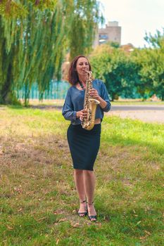 nice girl with red hair in a blue sweater and black skirt plays on the saxophone in the park