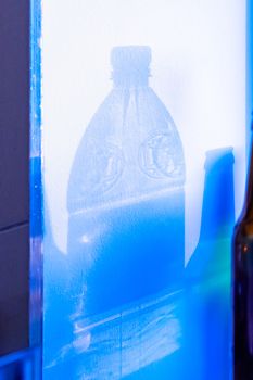 Projection of transparent shadows of an empty plastic bottle of water and an empty bottle of beer on a white wall