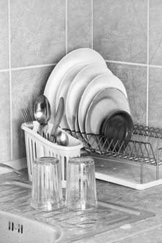 Washed plates, cutlery and glasses, drying in their racks close to the sink in the kitchen