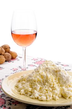 A nice plate of fresh homemade cheese on the table. A glass of rose' wine and some walnuts on the background