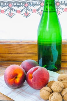 Three red peaches, a green glass bottle of wine and some walnuts, close to the window