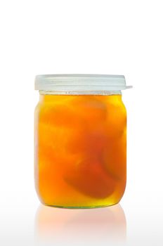 A jar of delicious homemade apricot jam with big pieces of fruit, on a white background, with reflection on the table