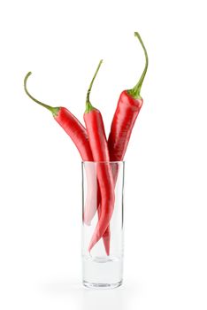 Three hot red chili peppers in a vodka glass, isolated on white background