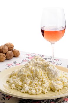 A nice plate of fresh homemade cheese on the table. A glass of rose' wine and some walnuts on the background