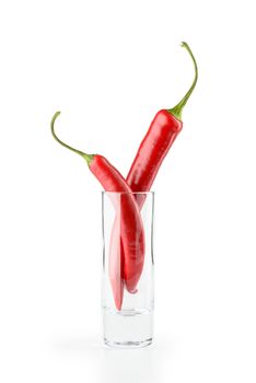 Two hot red chili peppers in a vodka glass, isolated on white background