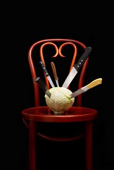 Symbolic conceptual image of a white cabbage on a wooden Thonet chair. Knives are stuck into the vegetable and symbolize cooking, violence, crime, suffering.  On black background.