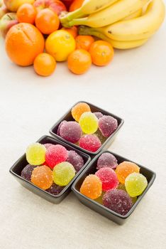 Colorful fruit jelly in little black ceramic cups. Fruits in the background