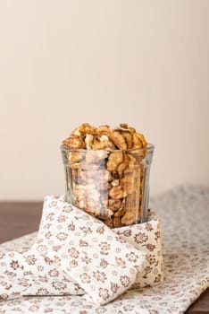 Fresh peeled walnuts in a glass on a wooden table with a white flowery tablecloth, and negative space for copy text