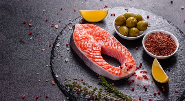 Raw trout red fish steak served with herbs and lemon and olive oil on a dark background. Cooking Salmon, sea food. Healthy eating concept