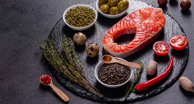Raw trout red fish steak served with herbs and lemon and olive oil on a dark background. Cooking Salmon, sea food. Healthy eating concept