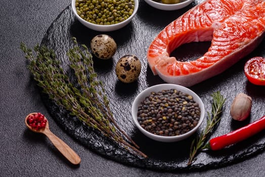 Raw trout red fish steak served with herbs and lemon and olive oil on a dark background. Cooking Salmon, sea food. Healthy eating concept