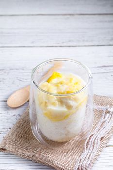 Summer appetizer of Thailand concept. Durian and sticky rice with coconut milk cream in transparent glass on white wooden table and brown table cloth. Famous street food in Thailand.  