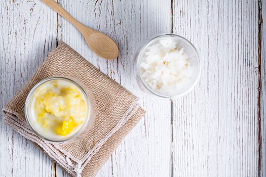 Summer appetizer of Thailand concept. Durian and sticky rice with coconut milk cream in transparent glass on white wooden table and brown table cloth. Famous street food in Thailand. Top view.  