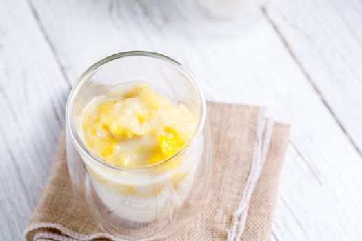 Summer appetizer of Thailand concept. Durian and sticky rice with coconut milk cream in transparent glass on white wooden table and brown table cloth. Famous street food in Thailand.  