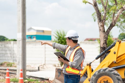 Asian man civil construction engineer worker or architect with helmet and safety vest working and holding a touchless tablet computer for see blueprints or plan at a building or construction site