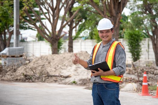 Asian man civil construction engineer worker or architect with helmet and safety vest working and holding a touchless tablet computer for see blueprints or plan at a building or construction site