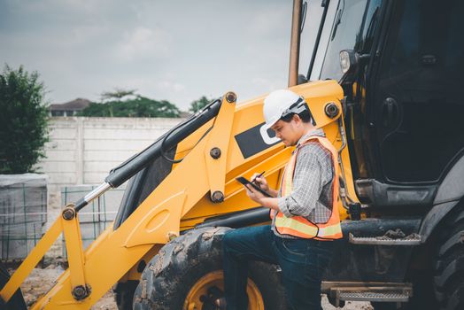 Asian man civil construction engineer worker or architect with helmet and safety vest working and holding a touchless tablet computer for see blueprints or plan at a building or construction site