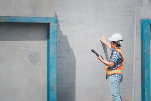 Asian woman civil construction engineer worker or architect with helmet and safety vest working and holding a touchless tablet computer for see blueprints or plan at a building or construction site