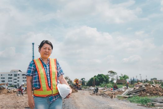 Asian woman civil construction engineer worker or architect with helmet and safety vest happy working at a building or construction site