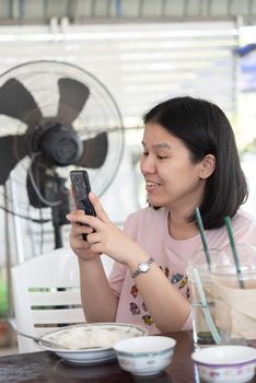 Asian woman foodstagramming use smartphone photographing a food on table in restaurant before eat for post and share on internet social media with fun and happy