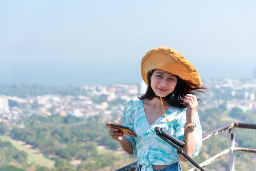 Asian pretty cute woman with hat relax and use smartphone at seaside city landscape viewpoint on mountain with happy and freedom emotion in concept travel, vacation, leisure in life