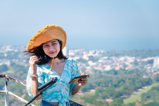 Asian pretty cute woman with hat relax and use smartphone at seaside city landscape viewpoint on mountain with happy and freedom emotion in concept travel, vacation, leisure in life