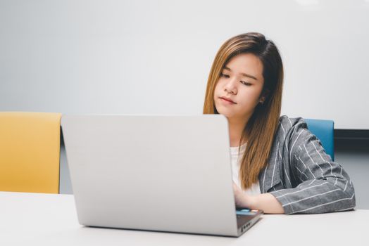 Asian woman is student, businesswoman working by computer notebook, laptop in office meeting room with whiteboard in background with happy and relax emotion in concept working woman, success in life