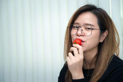 Asian pretty woman holding and eating fresh strawberry is red berry fruit color and sweet juicy with enjoy and happy emotion in concept food, healthy eating in life