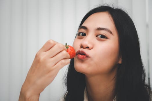 Asian pretty woman holding and eating fresh strawberry is red berry fruit color and sweet juicy with enjoy and happy emotion in concept food, healthy eating in life